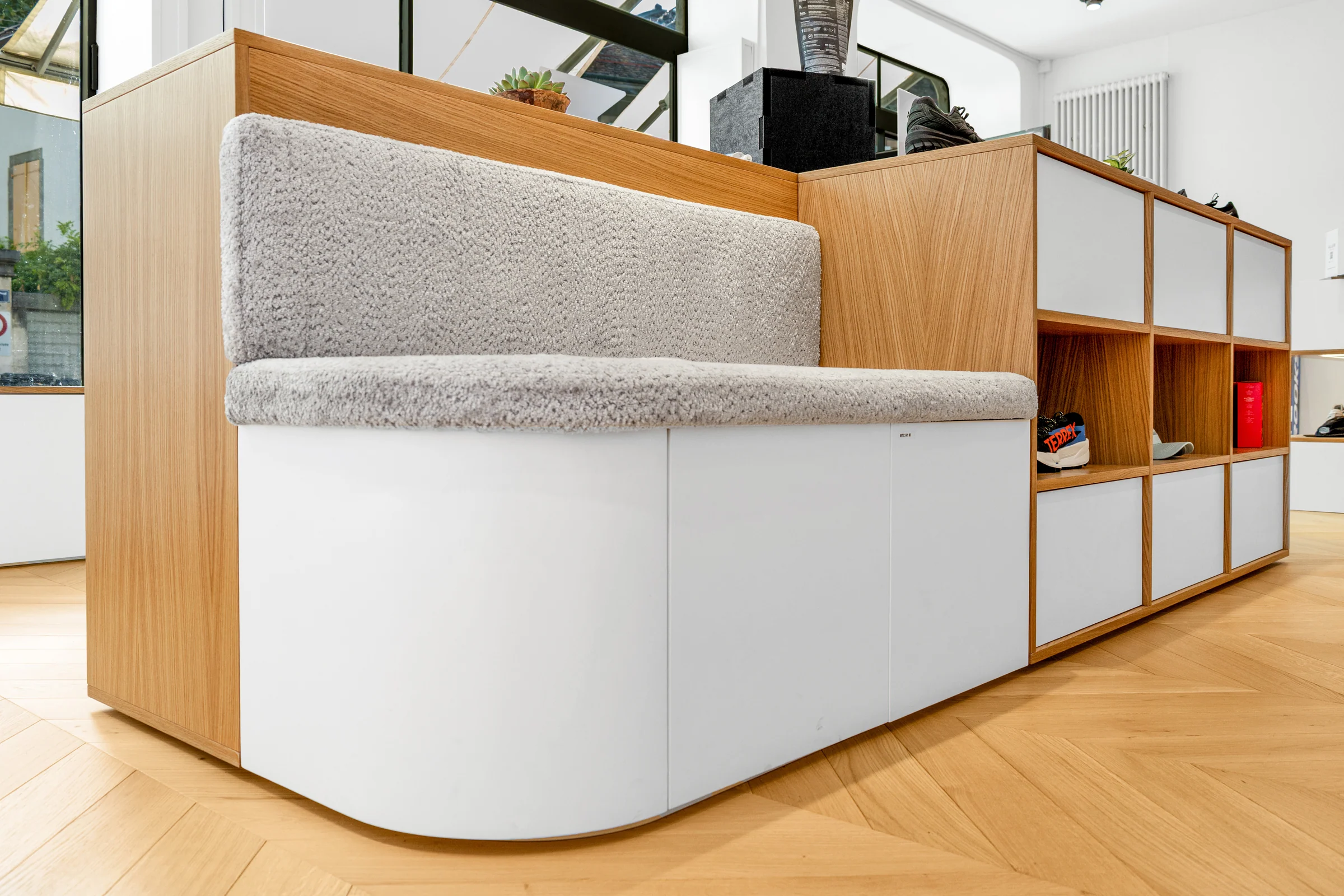 La banquette grise termine le meuble de rangement par une assise à l’extrémité arrondie.