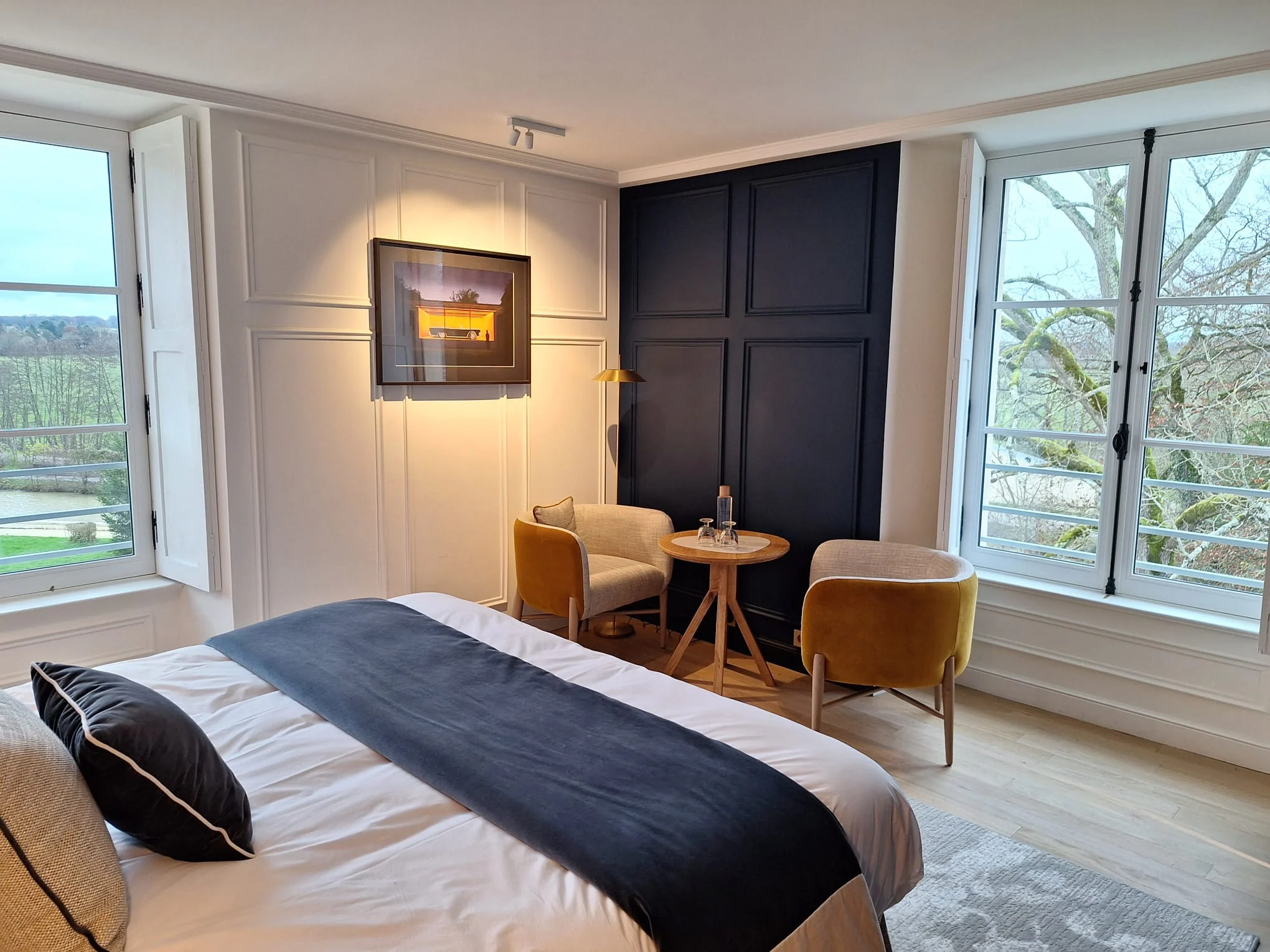 Chambre avec habillages muraux et espace assis près des fenêtres.