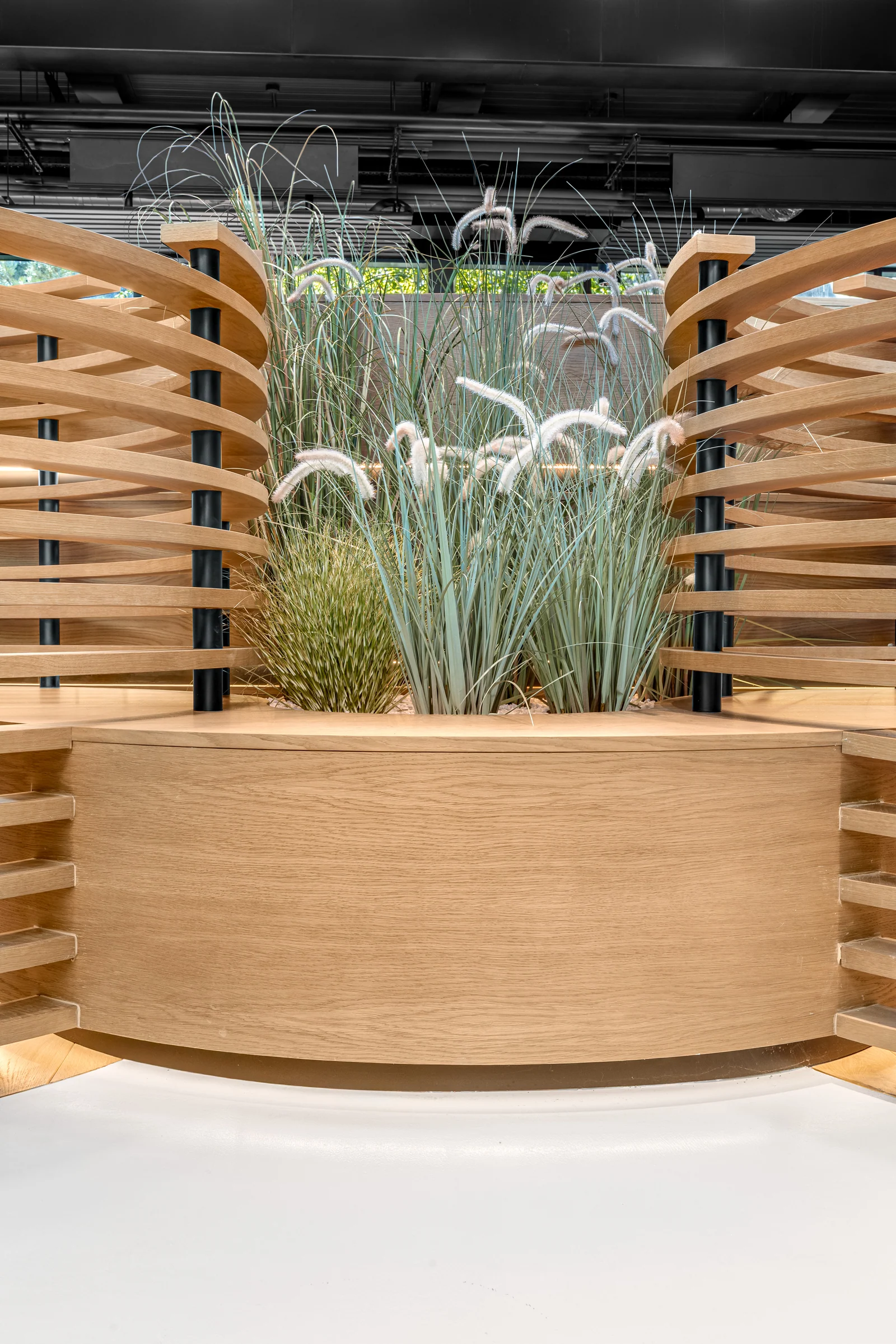Jardinière arrondie en bois entourée de cloisons courbes à lames horizontales.