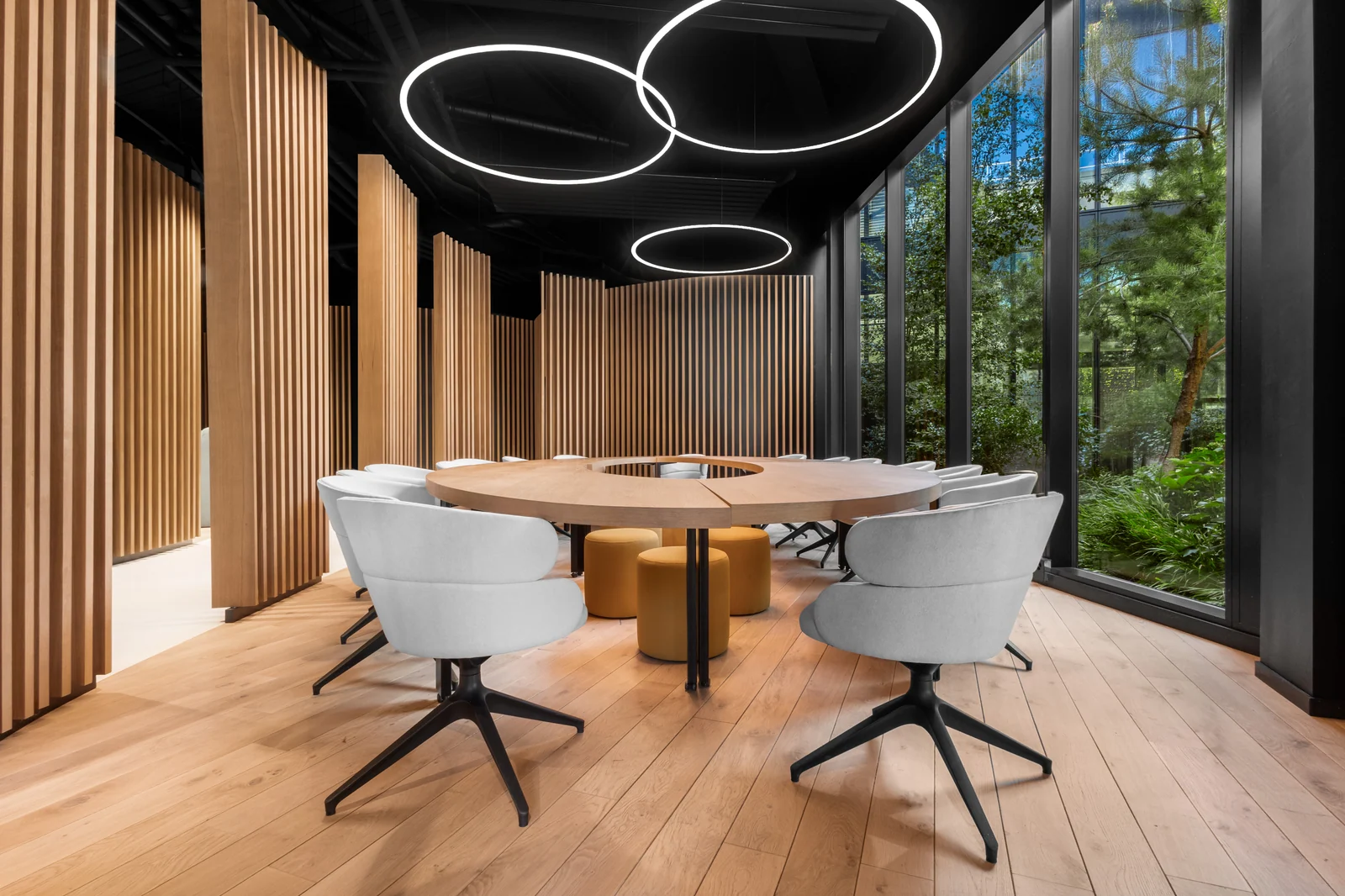 Table en bois avec fauteuils clairs dans la salle vitrée de Beezi à Tolochenaz, réalisation IAKO
