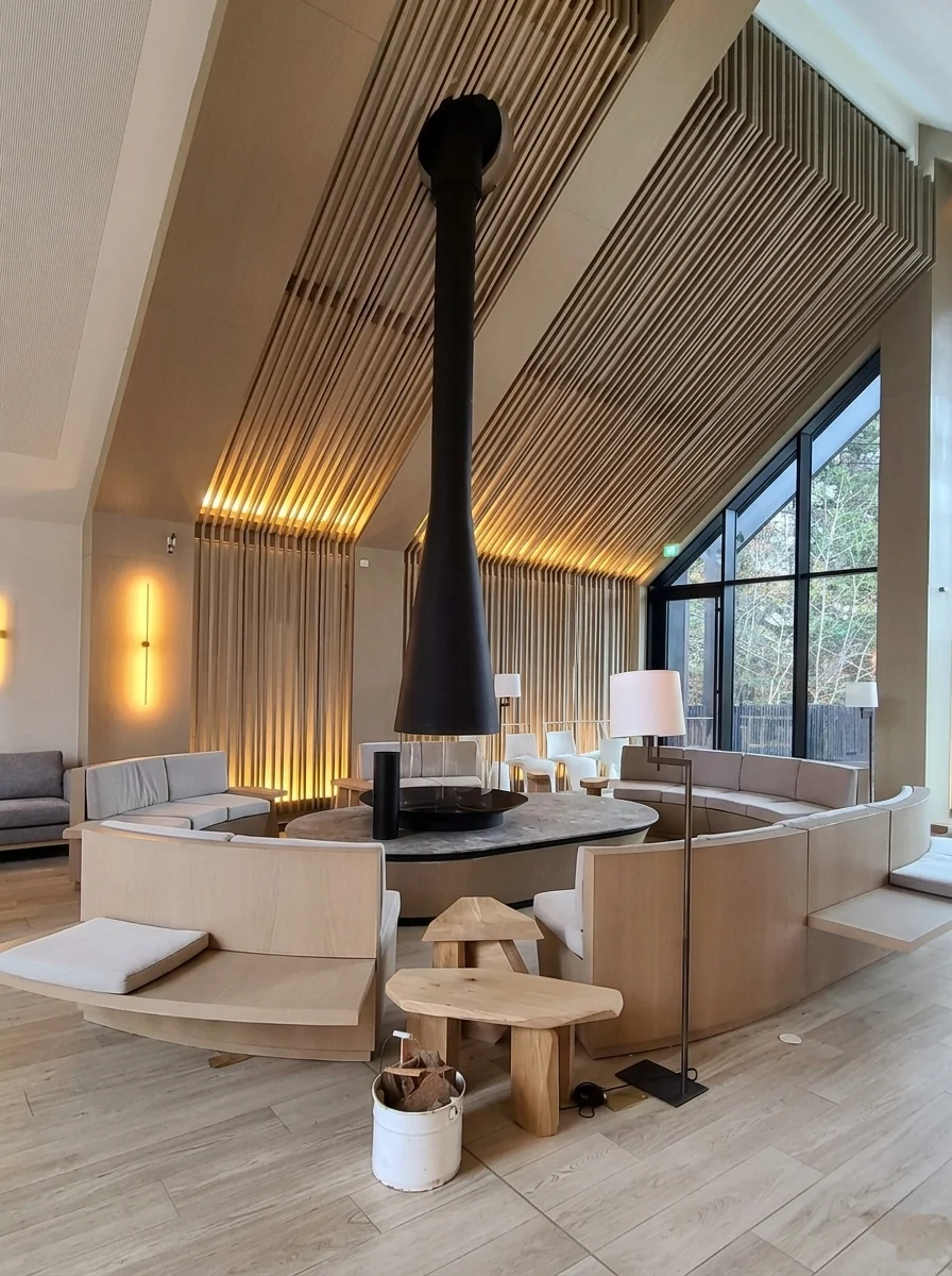 Salon IAKO : habillage en bois au mur et au plafond, mobilier disposé autour d’une cheminée