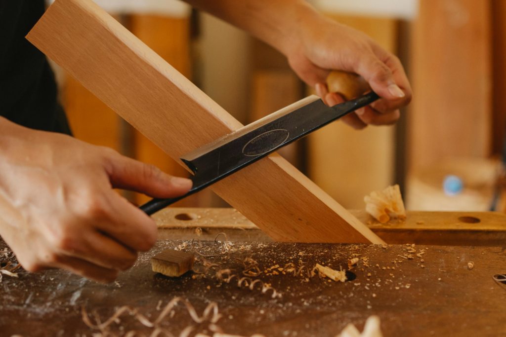 Close-up of a craftsman using a drawknife on wood in a workshop.